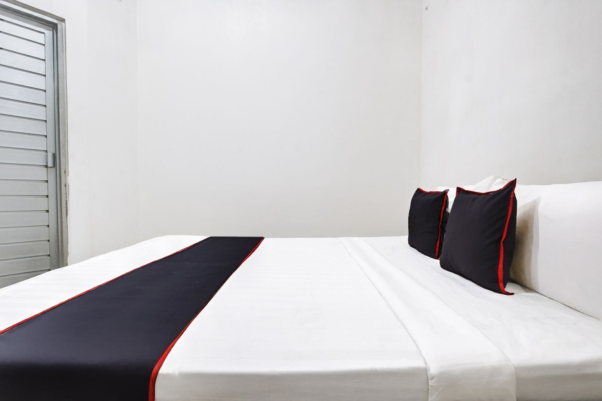 Ein Hotelzimmer mit Bett, weißen Wänden und einem Fenster mit Jalousien.