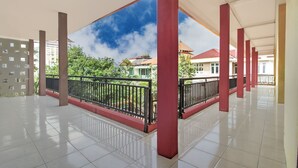 A spacious covered balcony area with tiled flooring and red pillars, offering a view of surrounding buildings and greenery. - Hotel O Oteng Stay (Semarang)