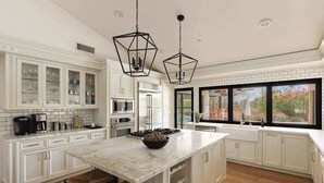 A modern kitchen with white cabinetry, a marble island, and pendant lighting.