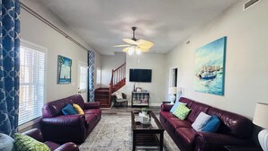 A living room with two leather sofas, a coffee table, a TV, a painting, and a staircase. - Boat & pet friendly. Minutes to Emerald Isle & a half mile to the boat ramp. (Cedar Point)