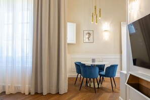 Ein moderner Essbereich mit einem runden Tisch und blauen Stühlen, einem Fernseher rechts und einem gerahmten Bild an der Wand.