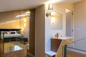 A modern hotel room with a glass partition separating the bed area from the bathroom.