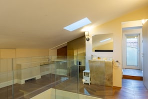 A spacious living area with a glass railing, a skylight, and a modern bathroom with a marble countertop.