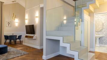 Un soggiorno moderno con una TV a schermo piatto, un'area pranzo con sedie e una scala con ringhiere in vetro.