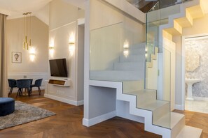 Ein modernes Wohnzimmer mit Flachbildfernseher, einem Essbereich mit Stühlen und einer Treppe mit Glastrennläufen.