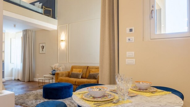 A modern living room with a round marble table, blue chairs, and a sofa with yellow cushions. - Calzaiuoli Gold Private House with Terrace (Firenze)