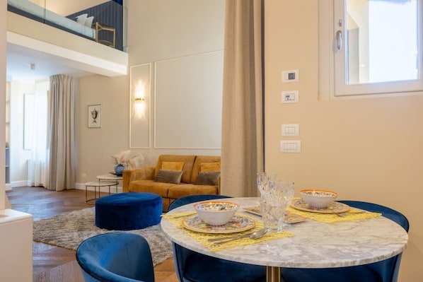 A modern living room with a round marble table, blue chairs, and a sofa with yellow cushions.