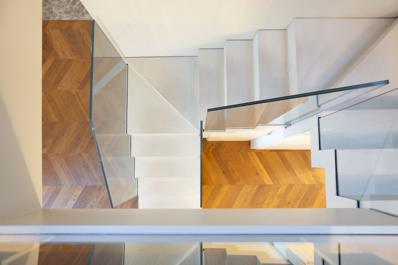 A modern staircase with glass railings and wooden flooring.