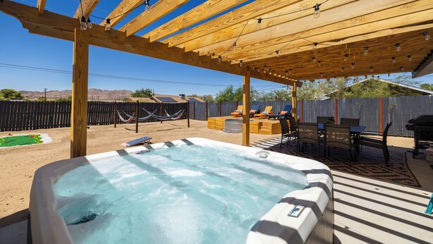 A hot tub under a wooden pergola with a clear blue sky in the background.