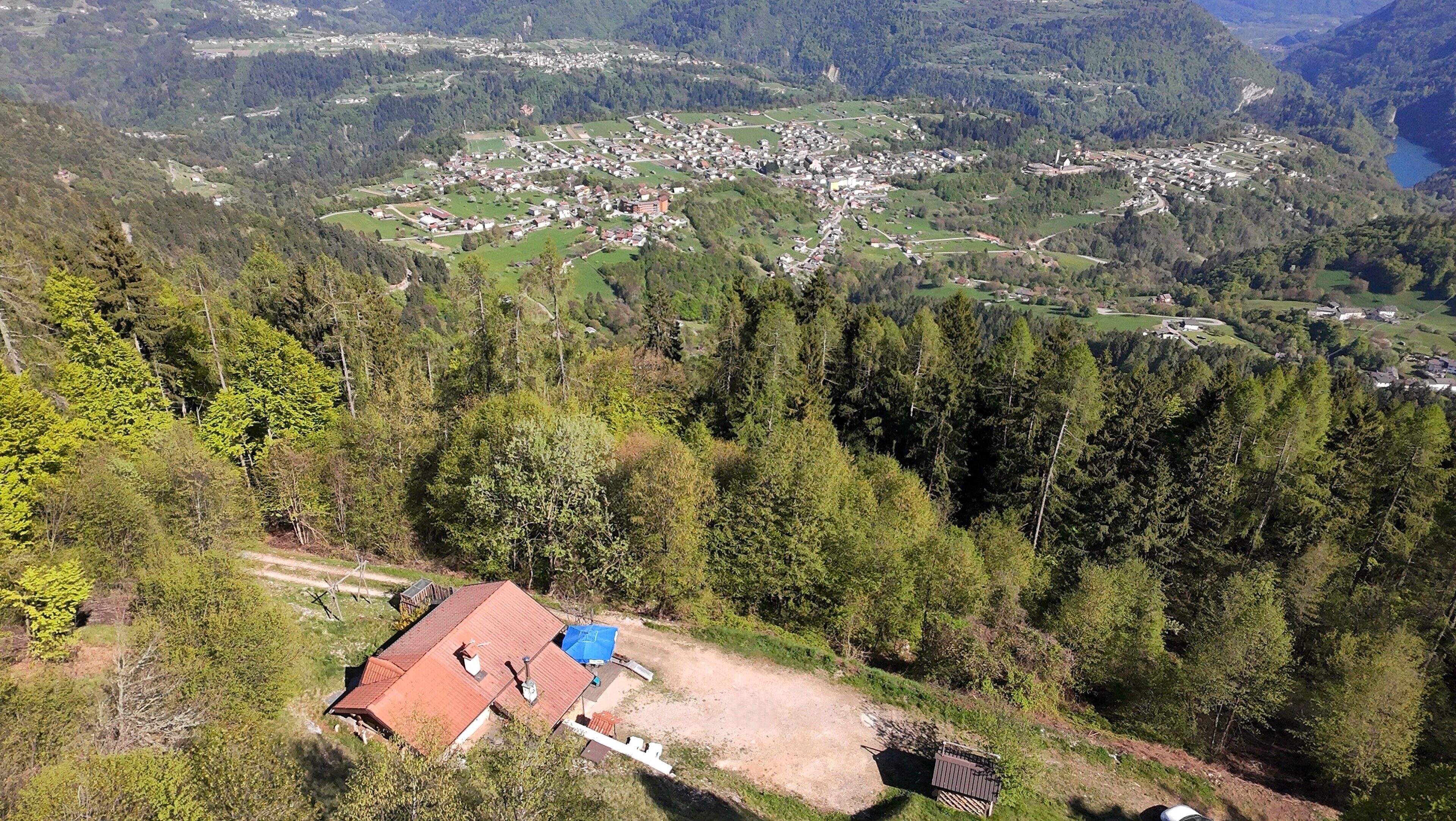 A rural village with a small building with a red roof, surrounded by dense forest and hills.