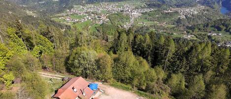 A rural village with a small building with a red roof, surrounded by dense forest and hills.