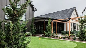 A modern building with a covered outdoor seating area, a well-maintained lawn, and surrounding greenery.