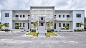 A modern building with a central entrance, balconies, and a parking lot. - Modern condo, steps to beach. Gym, generator, gated community. (Nassau)