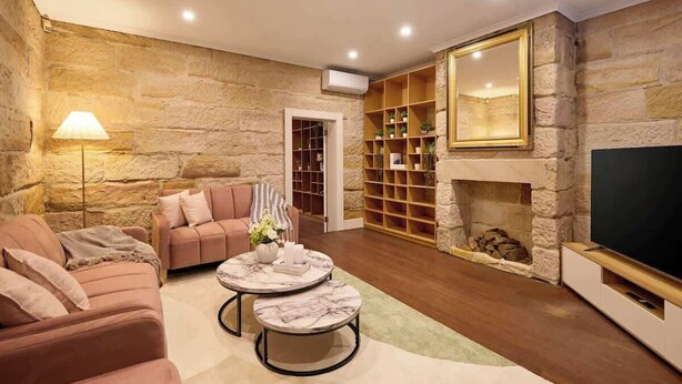 Una sala de estar con paredes de piedra, chimenea, televisor y estantería.