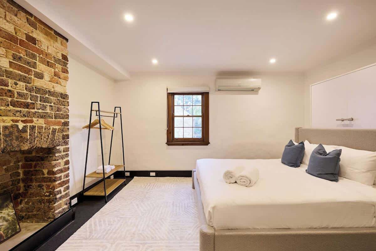 A bedroom with a brick wall, a bed with pillows, a window, and a hanging chair.