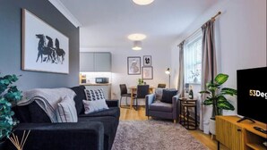 Een moderne woonkamer met een bank, een televisie en een eethoek op de achtergrond.