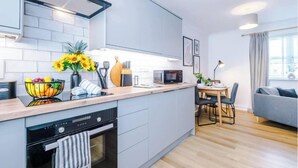 Een moderne keuken met een centraal eiland, een eethoek met een tafel en stoelen, en een grijze bank in een zithoek.