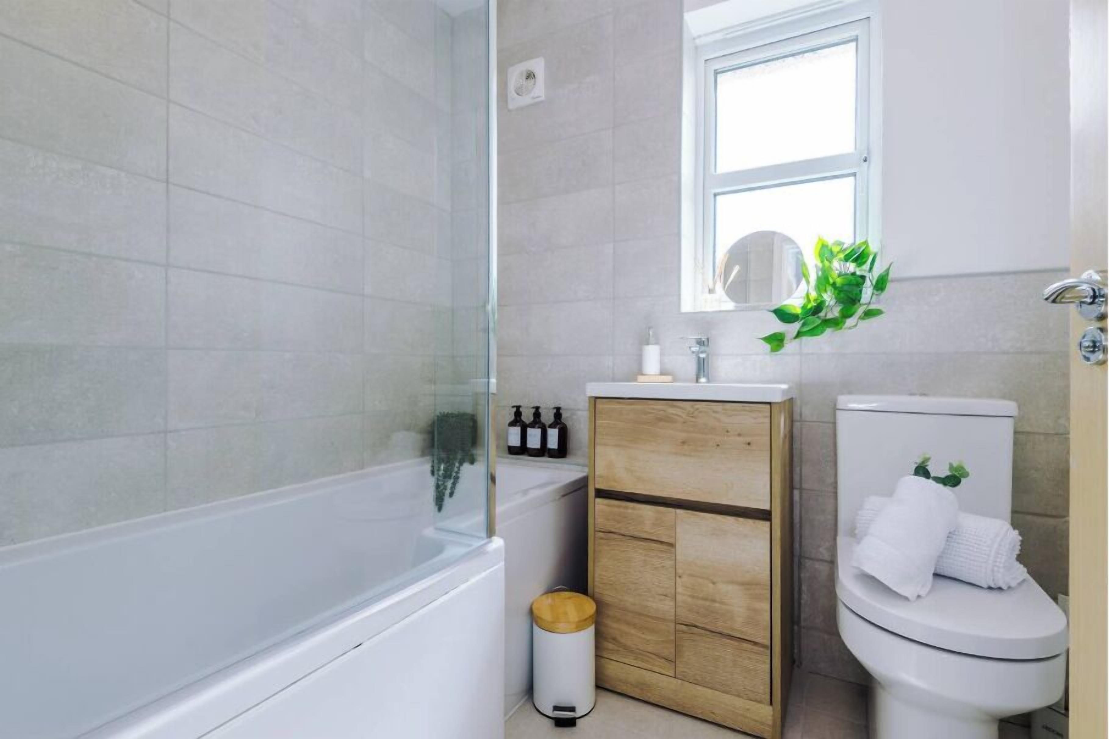 A modern bathroom with a glass-enclosed shower, a wooden vanity, and a toilet with a plant decoration.