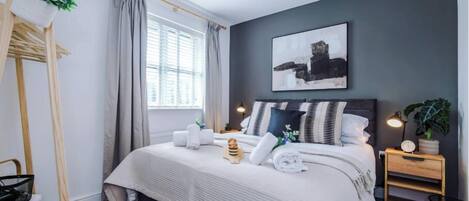 Un dormitorio moderno con cama, mesita de noche, lámpara y un cuadro en la pared.