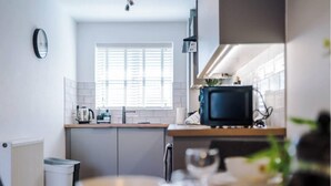 Een moderne keuken met witte kasten, een raam met zonwering, een kleine televisie en een radiator.