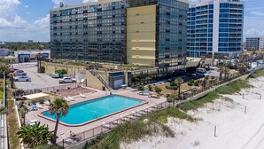 A modern hotel with a large glass facade, a swimming pool, and a beachside location.