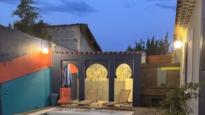 A swimming pool with a wooden deck, a potted plant, and a building with a tiled roof and arched windows. - BEAUTIFUL HOUSE IN PROVENCE (Avignon)