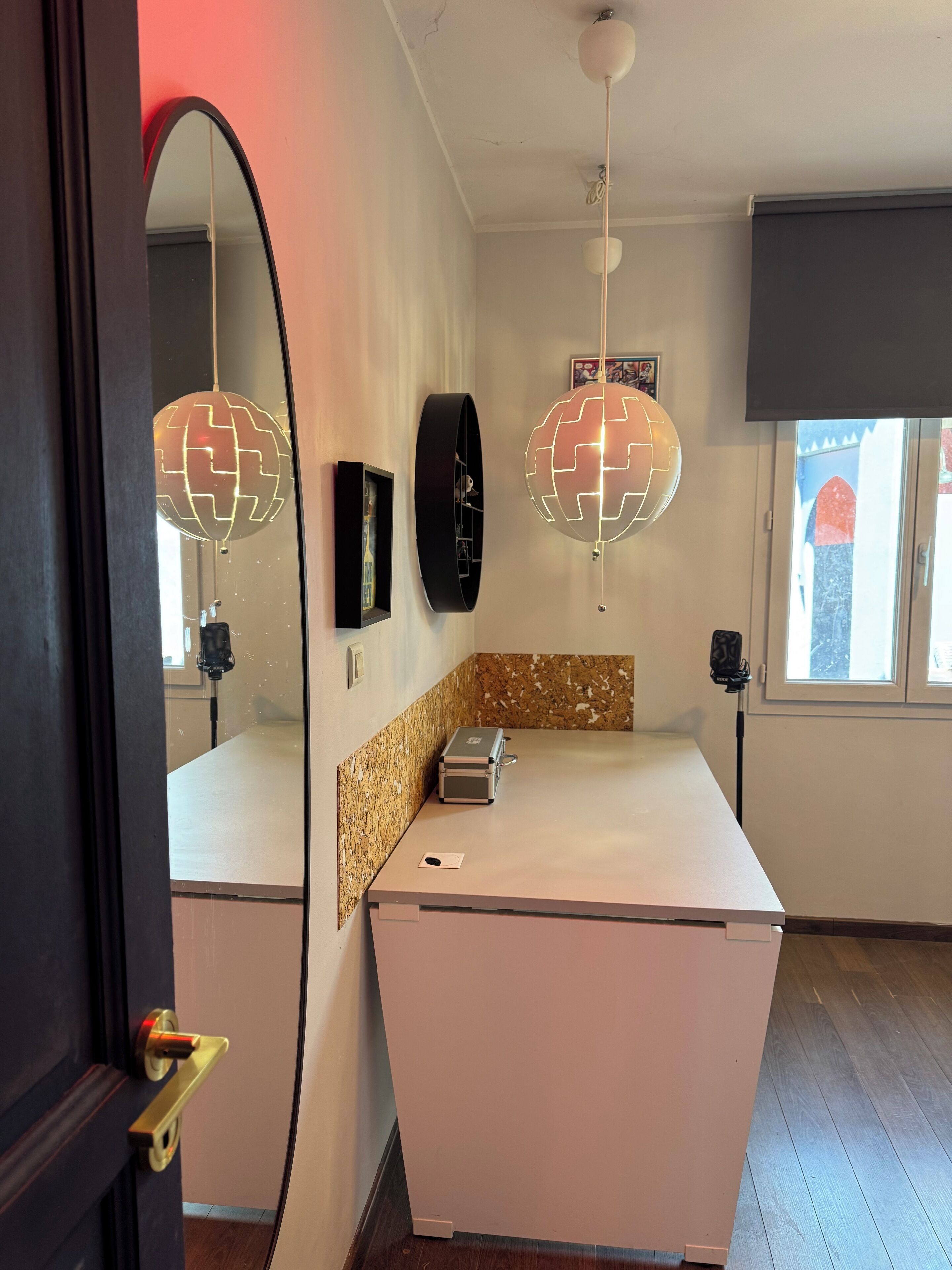 Ett modernt kök med en vit bänkskiva, en inbyggd ugn och en diskho i rostfritt stål. Det finns två hänglampor med en rund design, en svart klocka och en inramad tavla på väggen.
