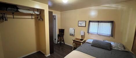 Een slaapkamer met een bed, een bureau, een stoel, een kapstok en een raam.