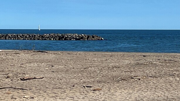 A beach with a rocky breakwater and a sailboat in the distance.
