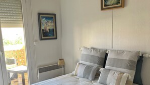 A bedroom with a bed, pillows, a painting, and a view of the outside.
