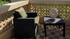 A balcony with a checkered floor, wicker furniture, and a decorative metal vase.