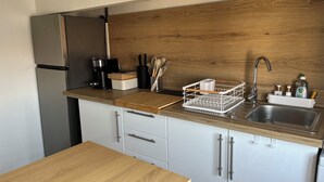 A modern kitchen with a stainless steel refrigerator, a wooden countertop, a sink with a faucet, and a dish rack.