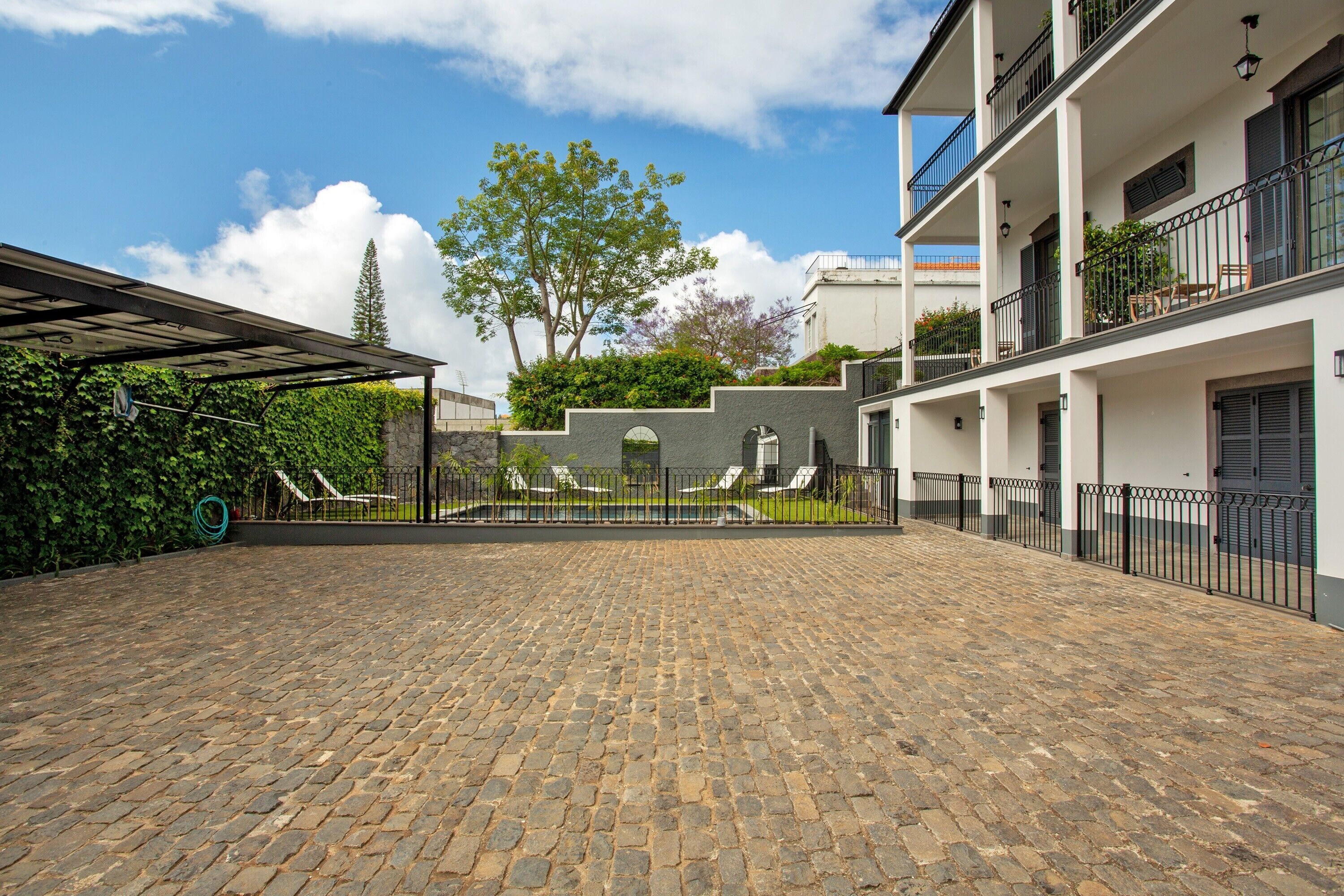 Une cour dallée de pierres, un espace de repos abrité et un bâtiment doté de balcons et de fenêtres.