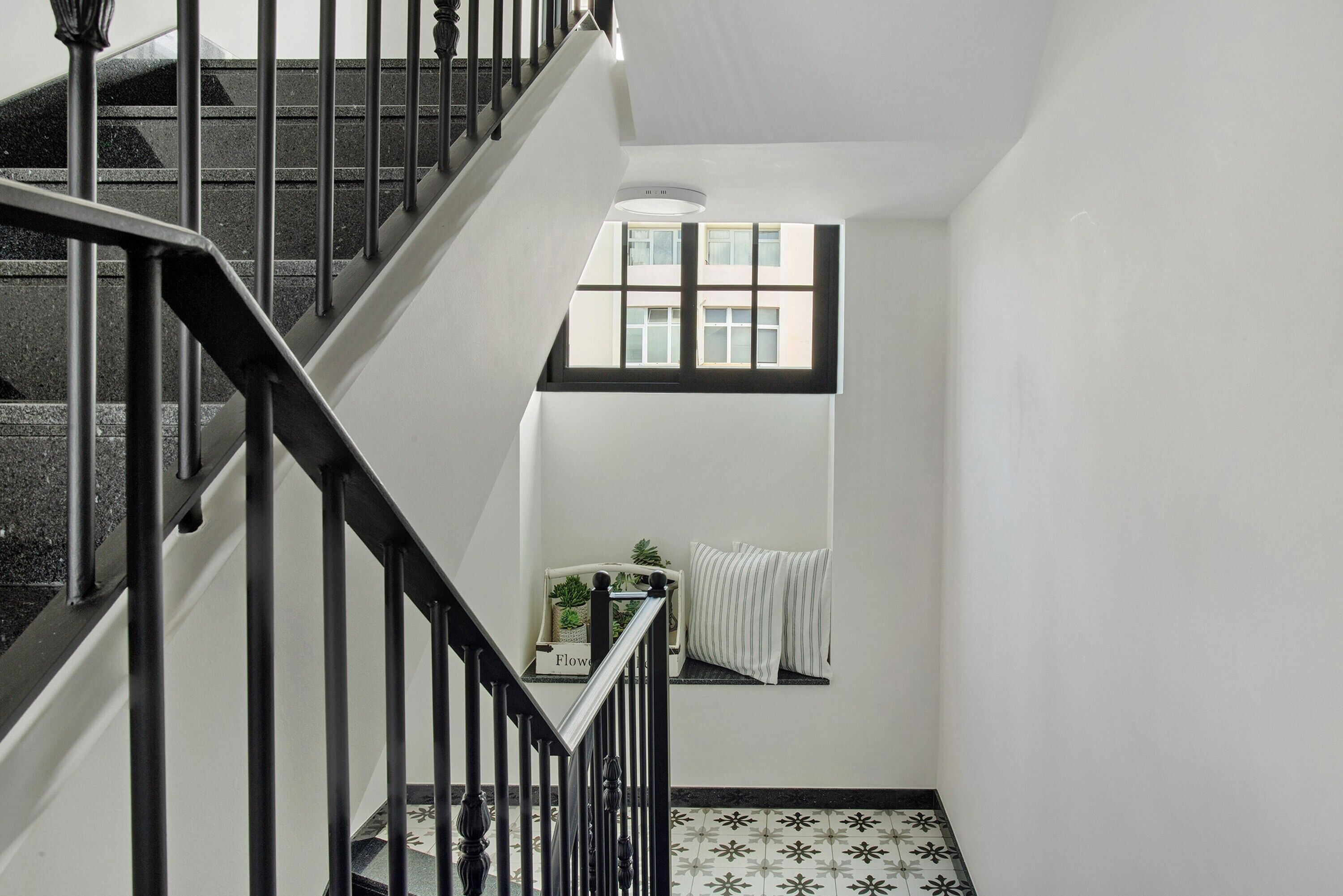 Un escalier avec des rampes noires, une fenêtre donnant sur des immeubles et un radiateur fixé au mur.