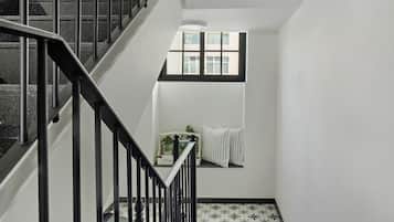 Un escalier avec des rampes noires, une fenêtre donnant sur des immeubles et un radiateur fixé au mur.