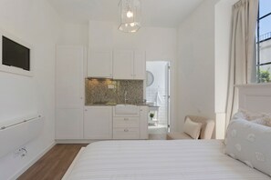 A bedroom with a bed, a small kitchenette, a window with curtains, and a door leading to another room. - Studio Apartment '1' with Shared Pool, Shared Garden and Wi-Fi (Funchal)