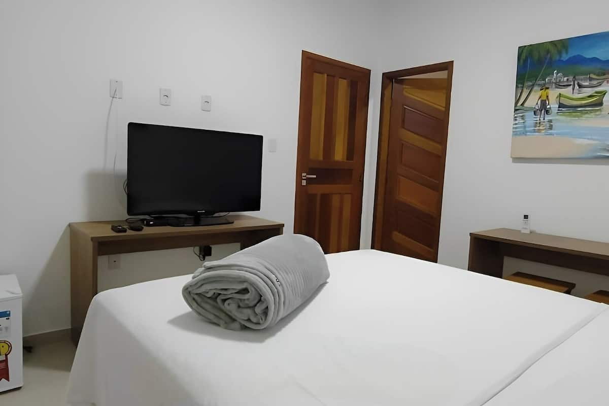 A hotel room with a bed, a television on a wooden stand, and a painting on the wall.