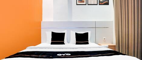 Quarto de hotel moderno com uma cama, dois travesseiros, uma mesa de cabeceira e um criado-mudo. Há três obras de arte emolduradas na parede.