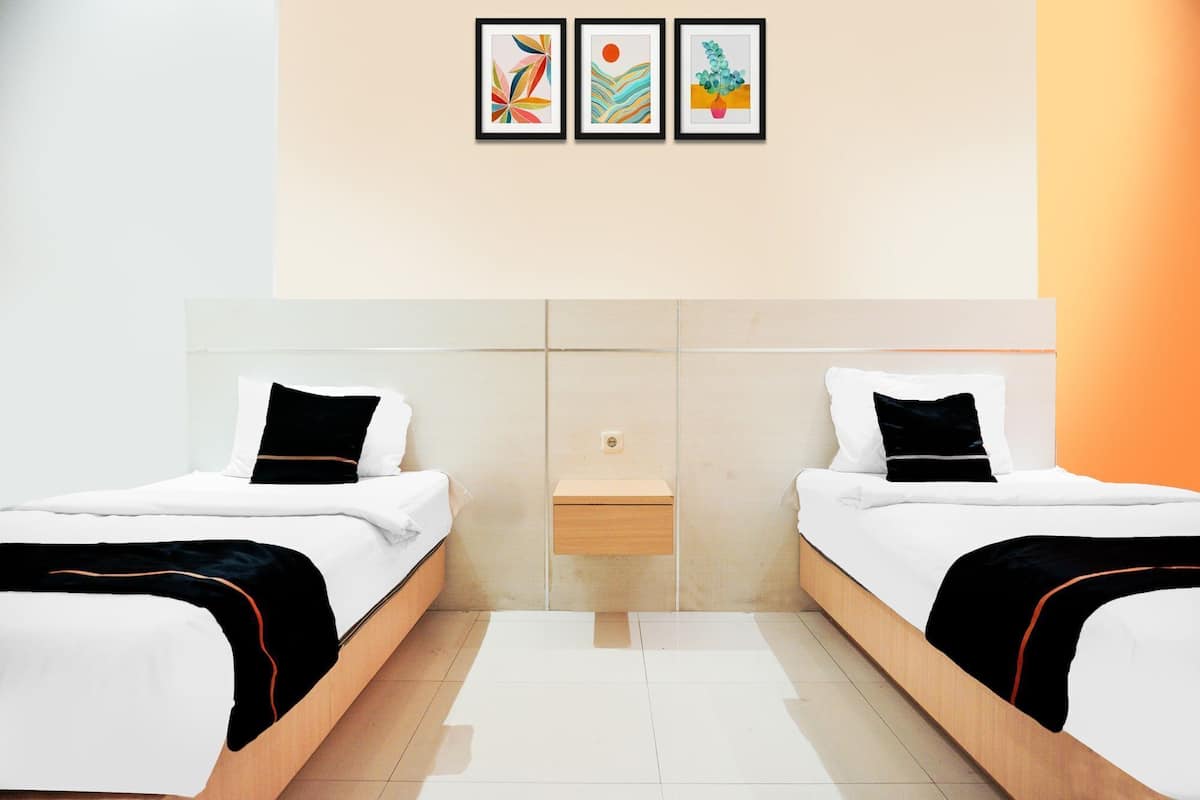 Une chambre d’hôtel avec deux lits, une petite table de chevet et trois œuvres d’art encadrées accrochées au mur.