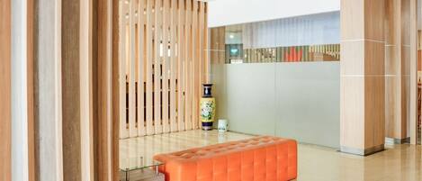 A modern lobby with a wooden partition, a glass table, and an orange bench.