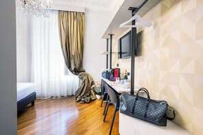 Ein Hotelzimmer mit einem Bett, einem Schreibtisch mit Stuhl, einem Fernseher und einer Handtasche auf einer Bank.