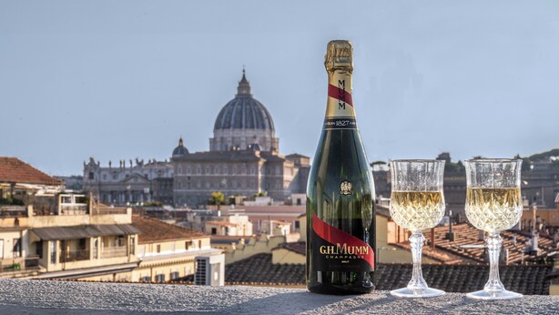 A bottle of G.H. Mumm Champagne and two glasses on a balcony with a cityscape and a dome in the background.