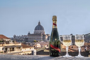 A bottle of G.H. Mumm Champagne and two glasses on a balcony with a cityscape and a dome in the background. - Gracchi Vatican View (Rome)