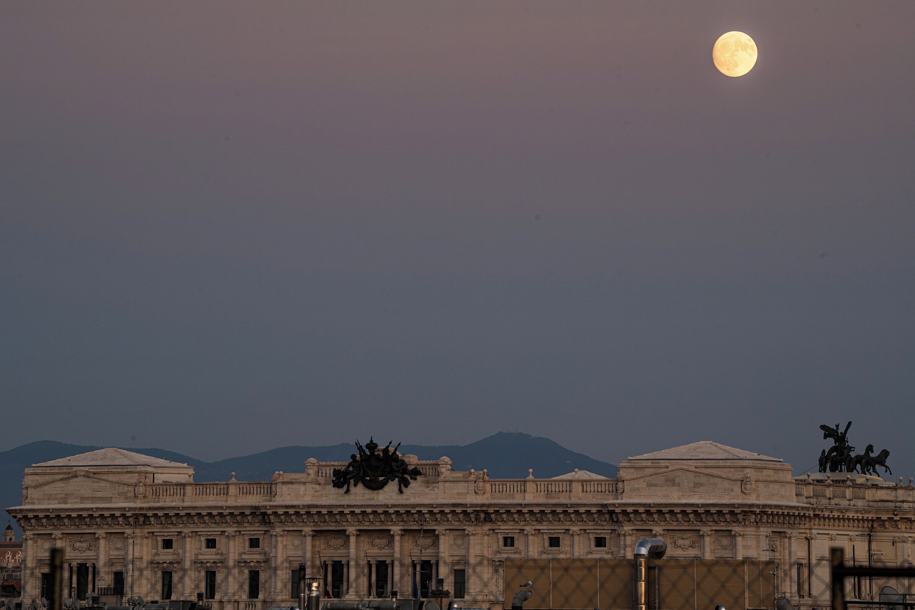 Un edificio imponente con arquitectura clásica, una estatua destacada en el techo y una luna llena en el cielo.
