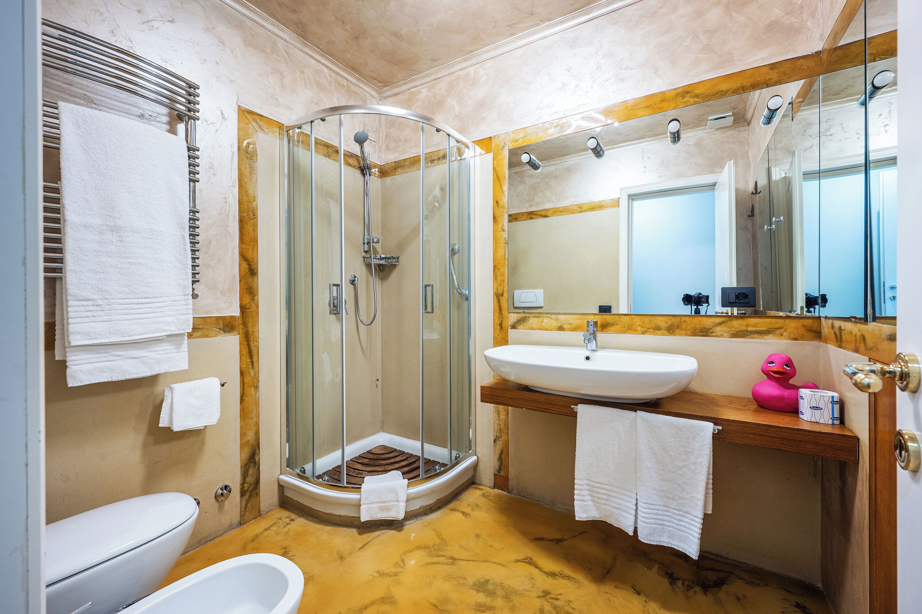 A bathroom with a glass-enclosed shower, a white sink, a wooden vanity, and a white toilet.