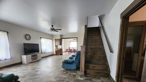 Un salon spacieux avec un téléviseur à écran plat, un canapé bleu et un escalier en bois.