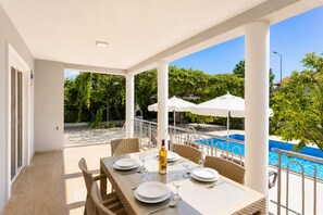 A covered outdoor dining area with a pool view, wicker chairs, and a table set for two.