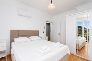 A bedroom with a bed, bedside tables, a mirror, and a balcony with a view.