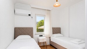 A small, clean room with two beds, a window with a view, a bedside table, and an air conditioning unit. - Daisy Villa - Five Bedroom Villa, Sleeps 10 (Dalyan)