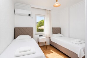 Ein kleines, sauberes Zimmer mit zwei Betten, einem Fenster mit Blick, einem Nachttisch und einer Klimaanlage.
